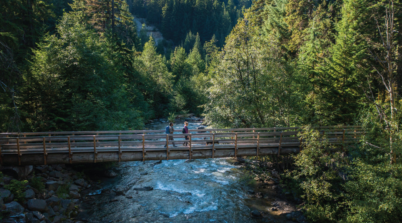 Two people crossing wooden bridge over river