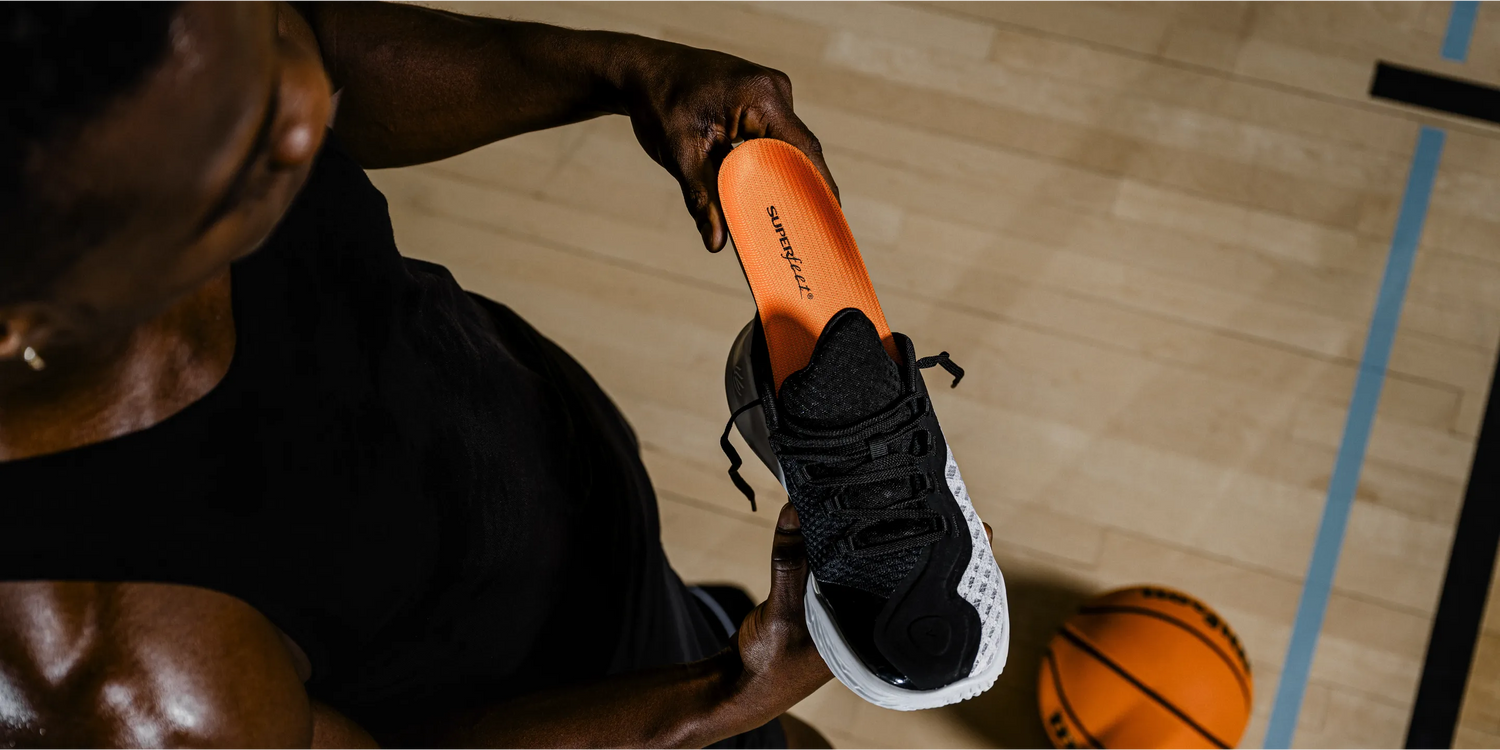 Man inserting Superfeet insole into athletic shoe on basketball court.