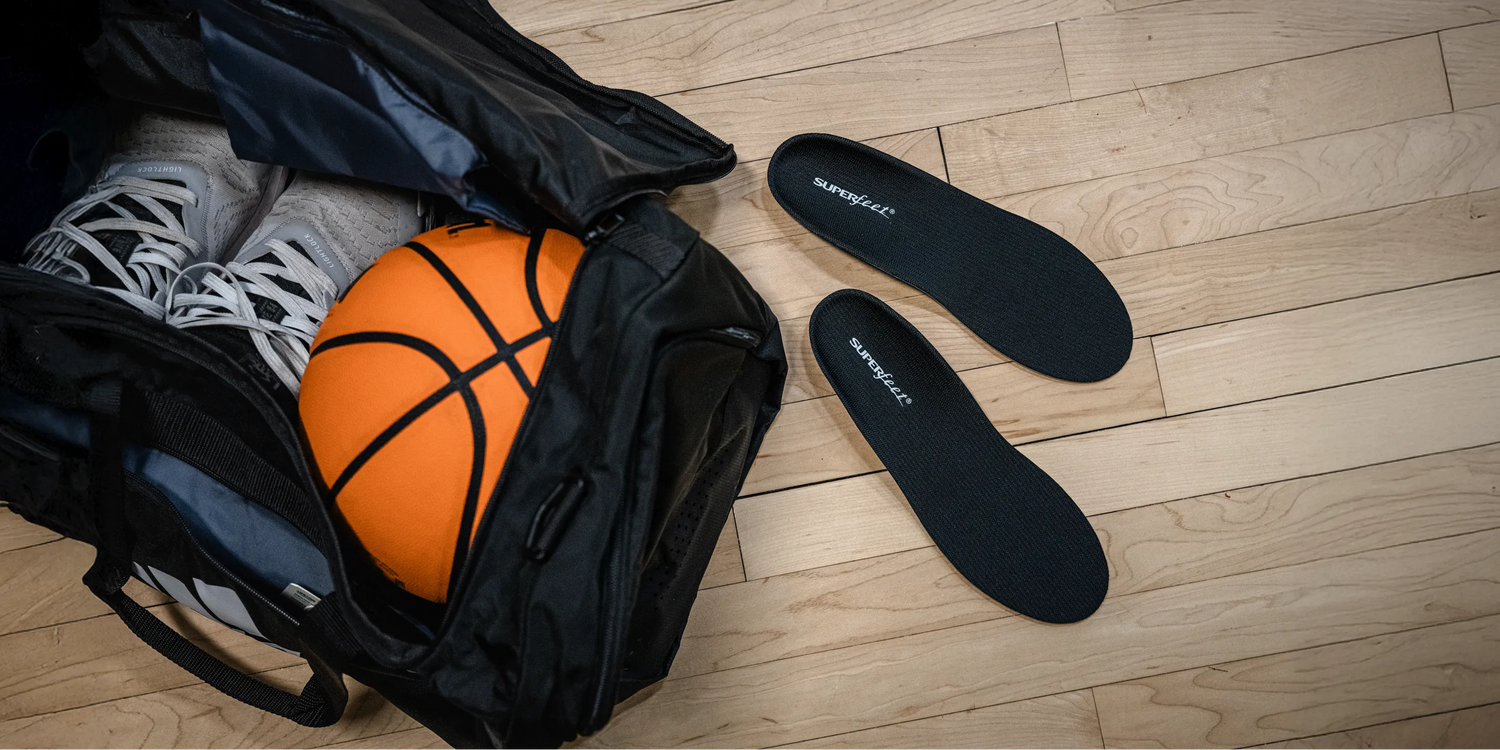 Image of a pair of Superfeet Support Low Arch insole on ground next to a gym bag with shoes and a basketball inside.