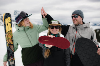 Three snow sport participants. The middle one holds a Superfeet insole up to the camera