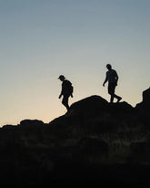 Silhouettes of two people wearing Superfeet insoles and hiking over rocky terrain as dusk approaches.