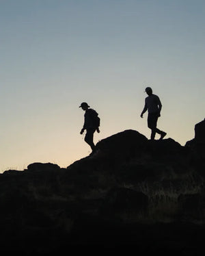 Silhouettes of two people wearing Superfeet insoles and hiking over rocky terrain as dusk approaches.