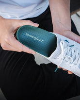 Man holding a white sneaker and inserting a Superfeet pain relief insole into his shoe.