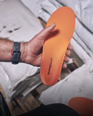 Man in warehouse standing on a wooden pallet with packages on top holding a Superfeet Work Orange insole.