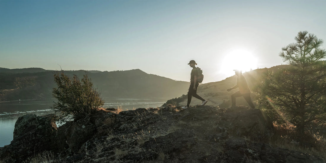 Two people wearing Superfeet insoles, hiking outdoors on a mountain ridge that overlooks the water.