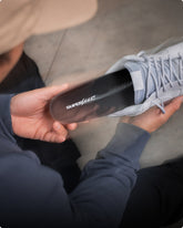 Person holding a light blue sneaker while inserting a  'Superfeet' insole against a blurred background.
