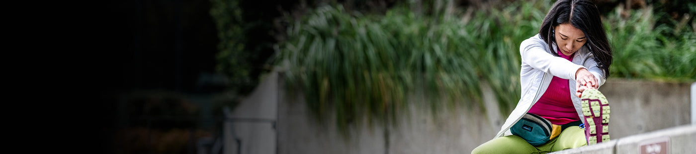 Woman sitting on a bench outside while stretching her legs and feet. 