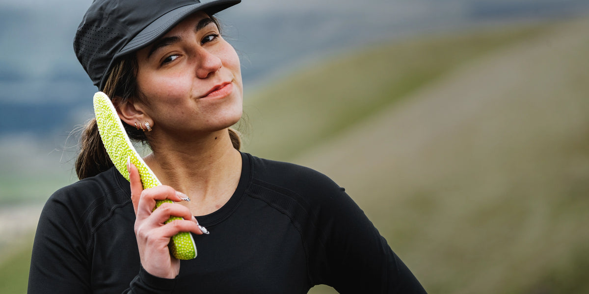A person is standing outside and holding Superfeet's Run Pacer Insole up to their ear like a telephone. 