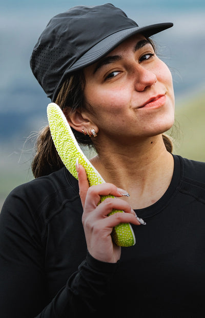 A person is standing outside and holding Superfeet's Run Pacer Insole up to their ear like a telephone. 