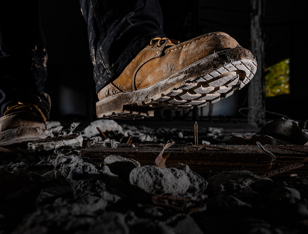 A close-up image of a person walking in an active construction zone, they are wearing a work boot & is about to step onto a nail. 