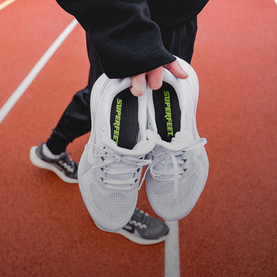 Someone standing on a track holding Superfeet's Run Pacer Insole inside of a white running shoe. 