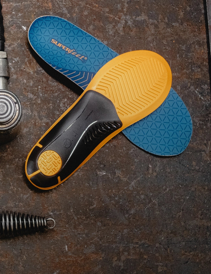 Superfeet's Work Slim-Fit Cushion Insole against a brown background with tools laying nearby. 