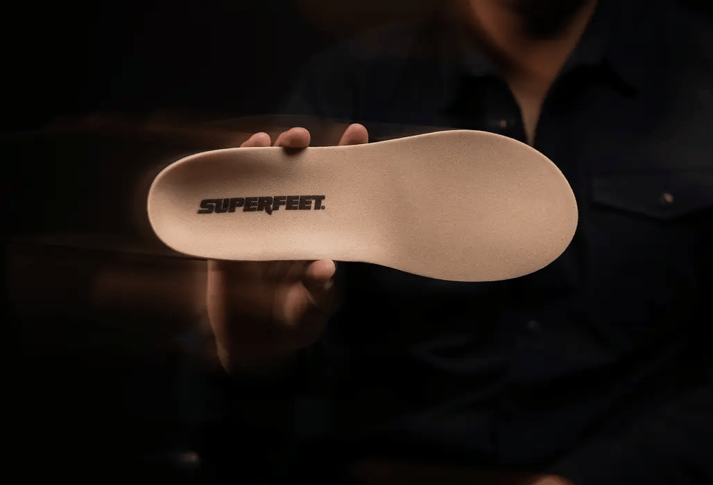 Superfeet insole held by a person against a dark background. 