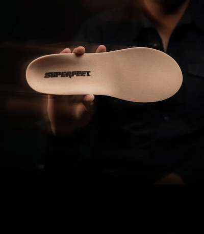 Superfeet insole held by a person against a dark background. 