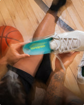Person inserting a blue 'Superfeet' insole into their white sneaker while sitting on the floor with a basketball in the background.