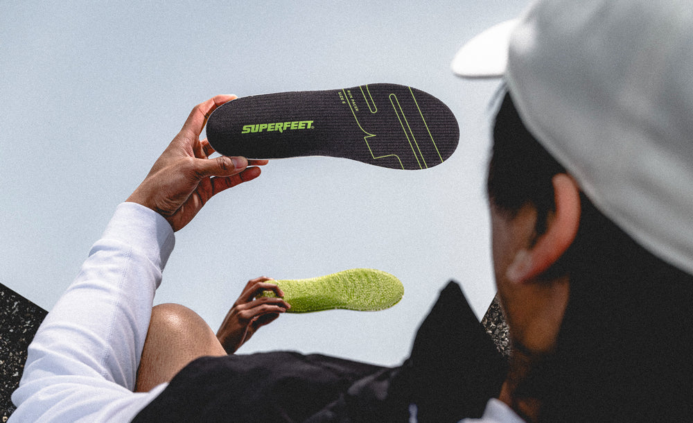 Person holding Superfeet insoles against a clear blue sky with a mirrored affect. 