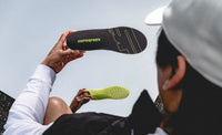 Person holding Superfeet insoles against a clear blue sky with a mirrored affect. 