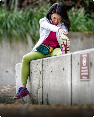 Woman stretching outdoors on a concrete ledge with greenery in the background