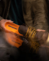 Someone inserting an orange 'Superfeet' insole into a a dark brown boot against a blurred background. 
