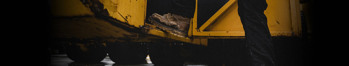 Close-up of a yellow vehicle's undercarriage with a person stepping up onto a platform. 