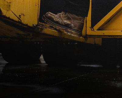 Person wearing work boots stepping out of a yellow container on a dark background. 