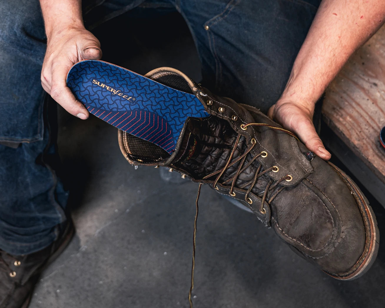 Person holding a brown leather boot and inserting a blue 'Superfeet" work insole into the boot
