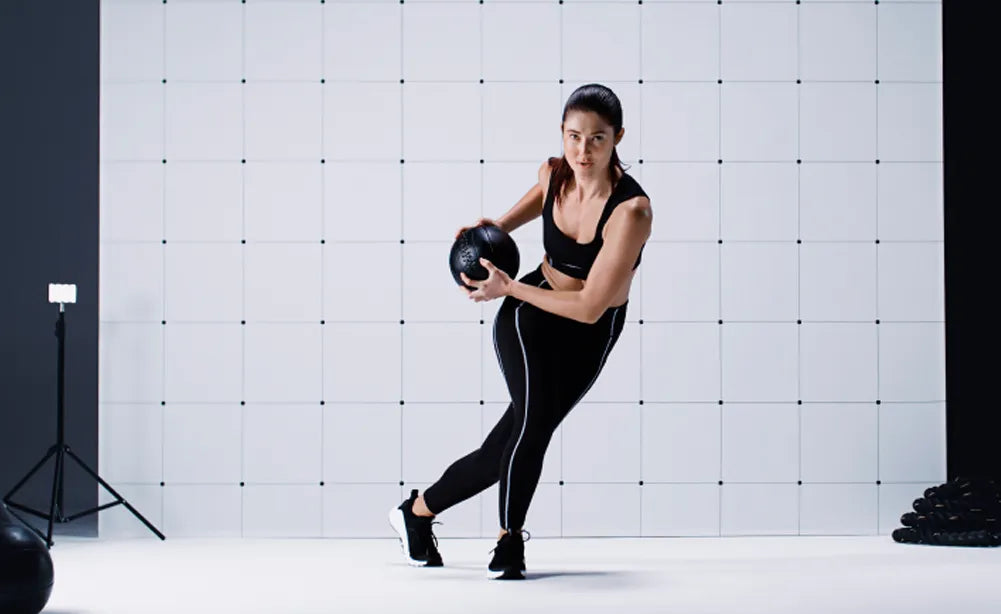 Woman in studio with a white background wearing all black and carrying a medicine ball while wearing Superfeet insoles.