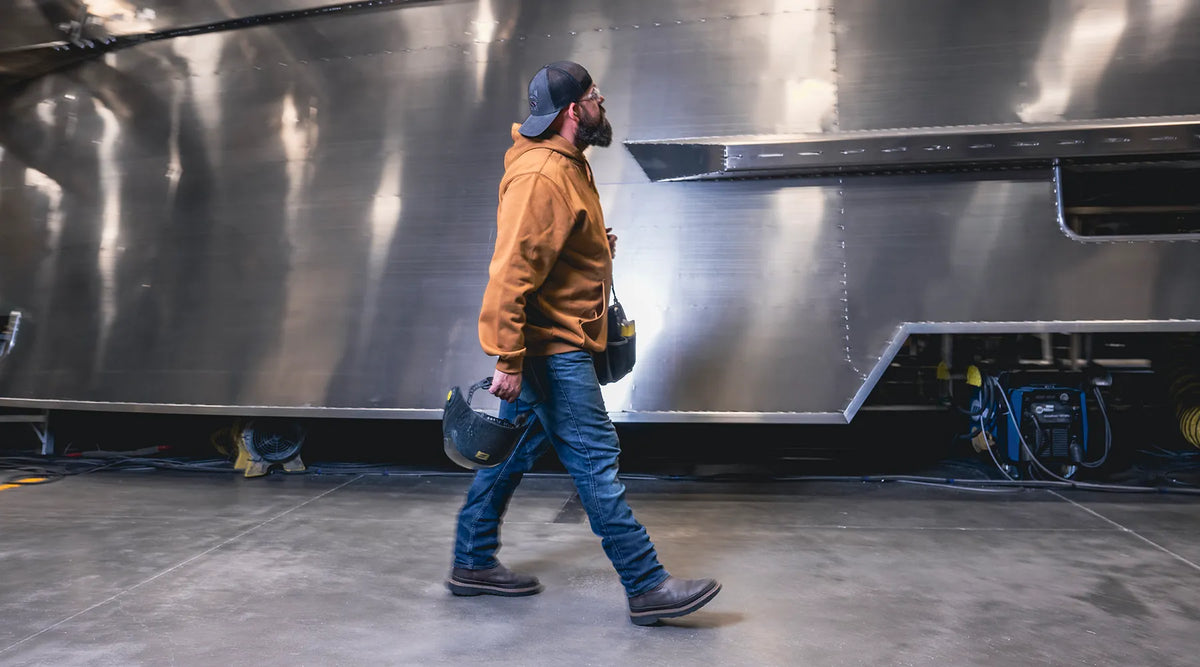 Man holding welding helmet walking past a large metallic object indoors while wearing Superfeet insoles 