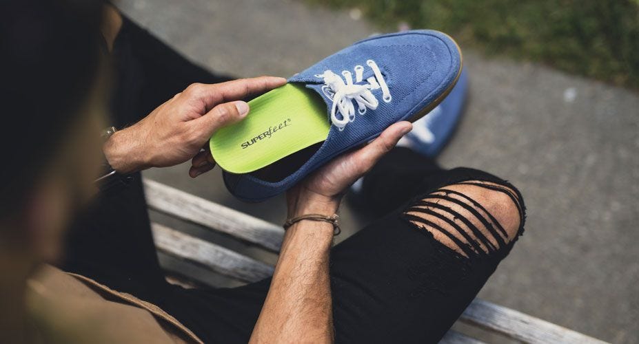 A man puts a Superfeet All-Purpose Support High Arch insole into his shoe.