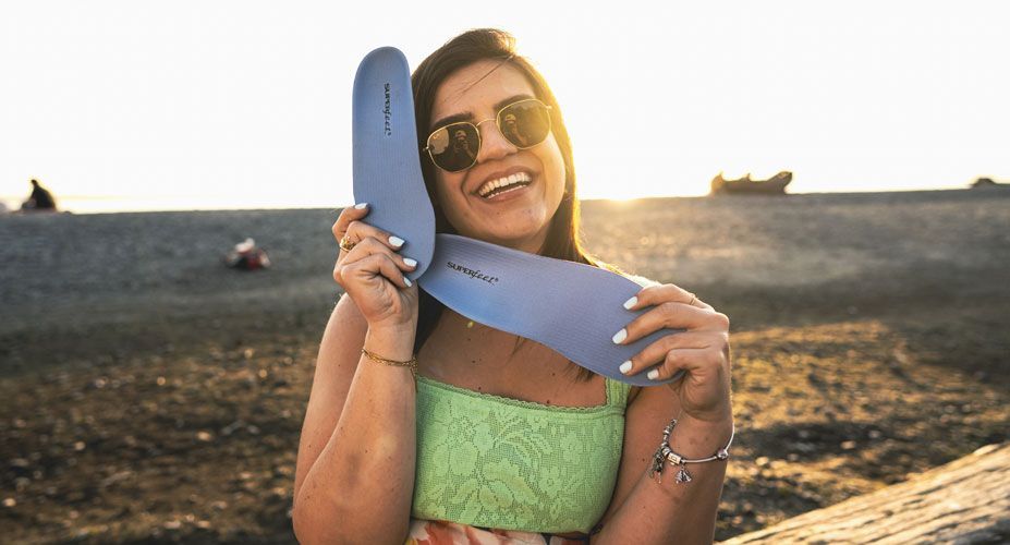 Woman wearing sunglasses smiles while holding Superfeet All-Purpose Support Medium Arch insoles.