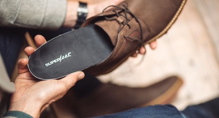 Man's hand putting Superfeet insole into brown dress shoe