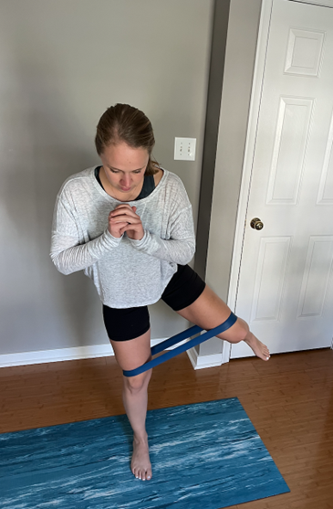 Woman balancing on one leg while lifting the other leg laterally. Exercise band around both legs, above the knee.