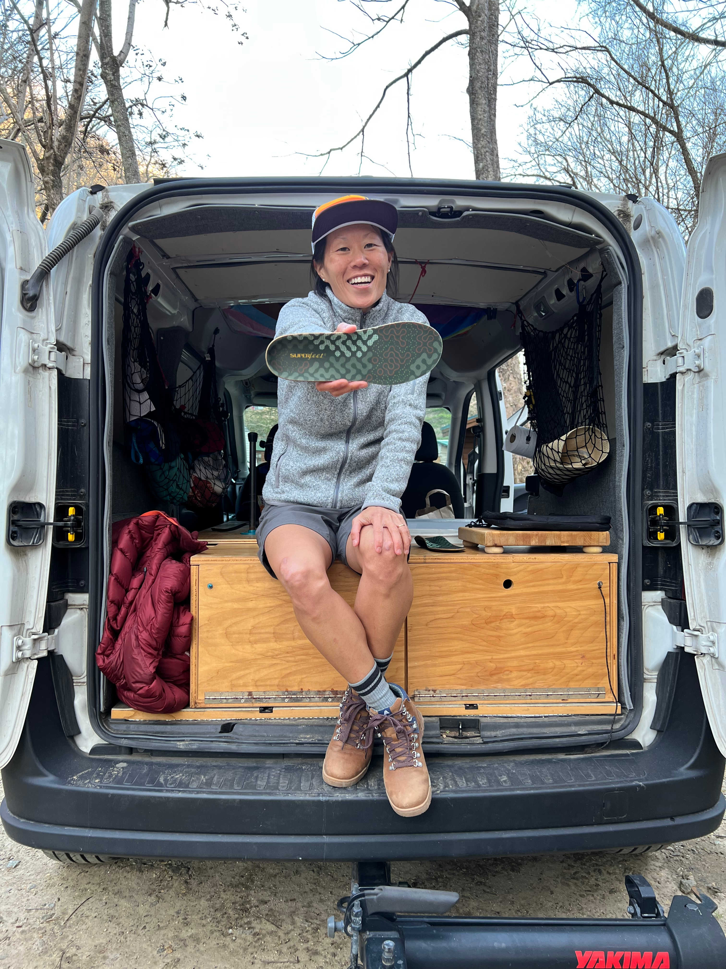 Hiker sits in the back of an adventure van and smiles at the camera while holding out a Superfeet ADAPT Hike Max insole