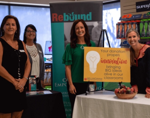 A group of women congregated at a trade show booth looking at the camera and smiling within a formal business environment.
