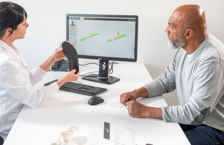 A practitioner engaged in conversation with a patient while holding an orthotic, discussing treatment options and solutions.