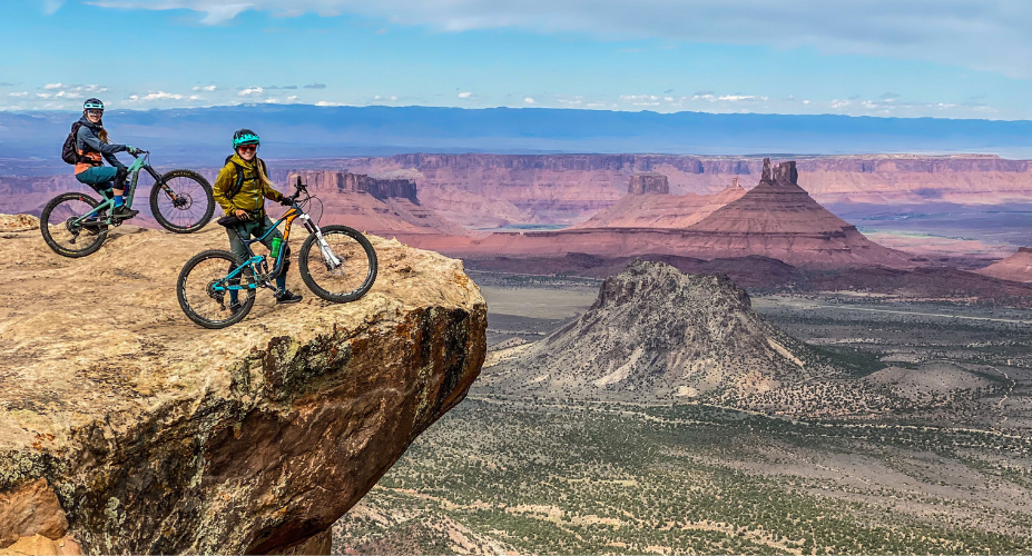 Two female mountain bikers on a ridge overlooking a desert landscape