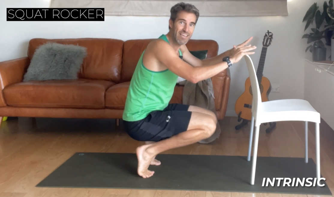 Runner holding onto a chair doing a stretch with graphic text overlay that says Squat Rocker