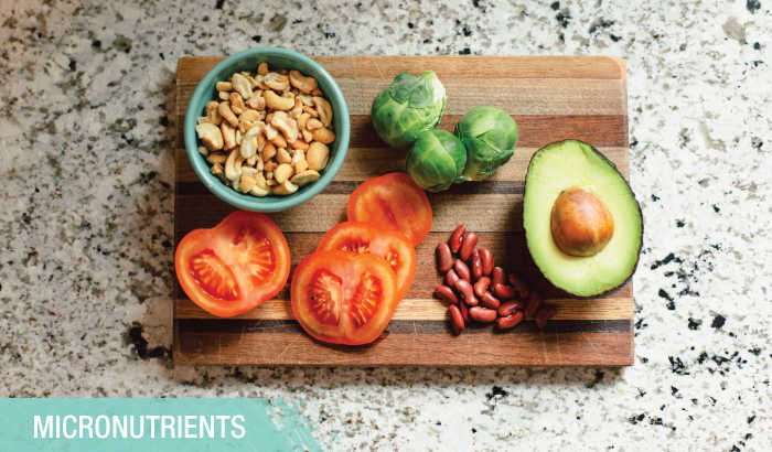 Nuts, sliced tomatoes, beans, sprouts and an avocado half on a wooden cutting board with a granite countertop background
