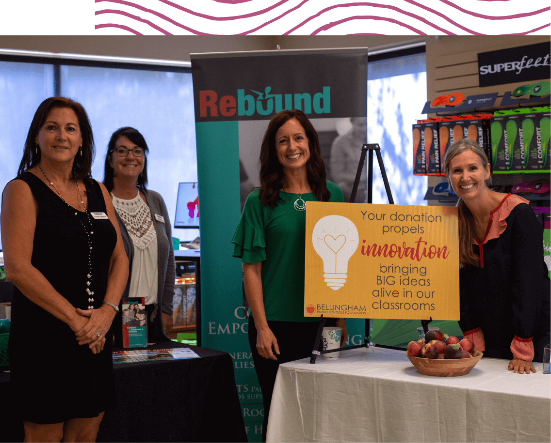 Four women standing behind a sign that says, "Your donation propels innovation bringing BIG ideas alive in our classrooms